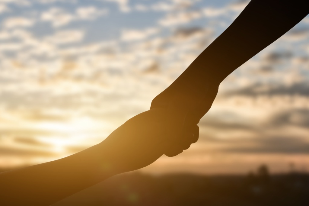 Silhouette of giving a help hand, hope and support each other over sunset background